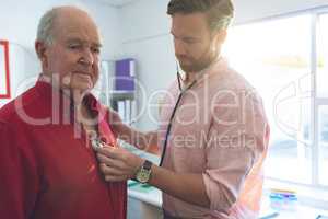 Confident male doctor checking senior patient heartbeats in clinic