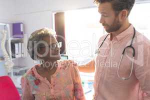 Confident male doctor interacting with female senior patient in clinic