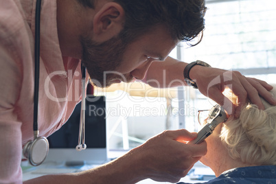 Male doctor checking senior female patient ear with otoscope