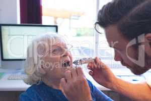 Male doctor checking senior female patient mouth with otoscope