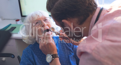 Male doctor checking senior female patient mouth with otoscope