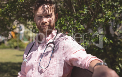 Confident male doctor sitting on bench outside the nursing home