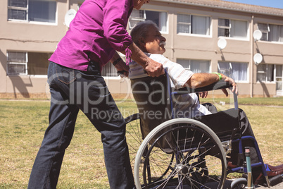 Senior woman pushing senior man on wheelchair at nursing park