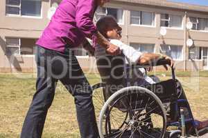 Senior woman pushing senior man on wheelchair at nursing park