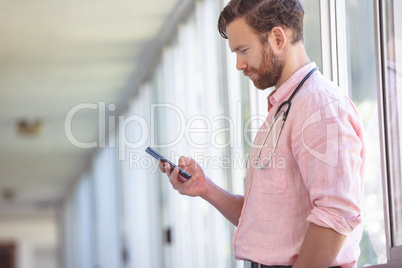 Male doctor using mobile phone while standing at nursing home corridor