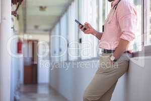 Male doctor using mobile phone while standing at nursing home corridor
