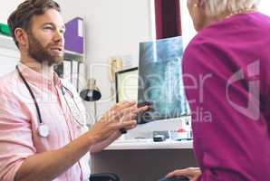 Male doctor showing x ray report to female senior patient in clinic