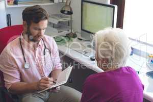 Male doctor writing prescription for senior woman in clinic room
