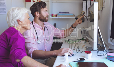 Male doctor showing medical reports on computer in a clinic room