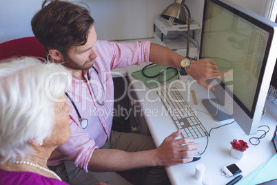 Male doctor showing medical reports on computer in a clinic room