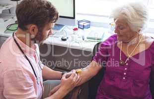 Male doctor giving an injection to senior female patient in clinic