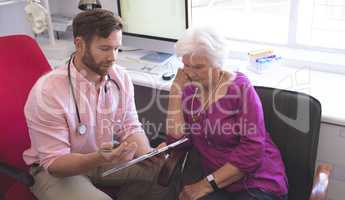 Male doctor showing prescription to senior woman in clinic room