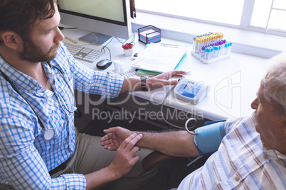 Male doctor checking blood pressure of senior patient
