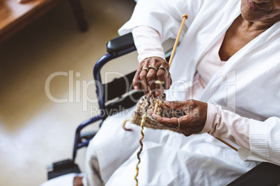 Senior woman sitting and knitting with wool at retirement home