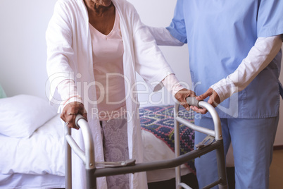 Female nurse helping senior female patient to stand with walker