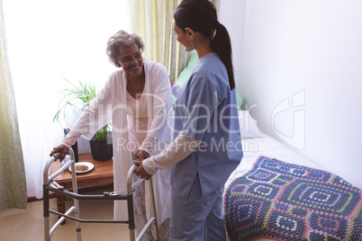 Female nurse helping senior female patient to stand with walker