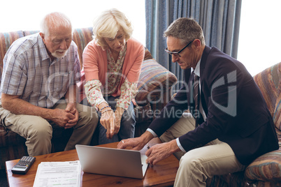 Matured male physician and senior couple discussing over laptop at retirement home