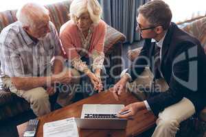 Matured male physician and senior couple discussing over laptop at retirement home