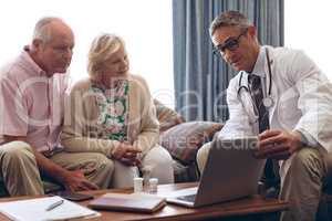 Male doctor discussing over laptop with senior couple at retirement home