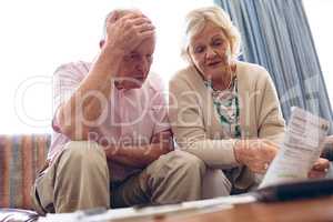 Senior couple discussing over medical bill while sitting on sofa at retirement home