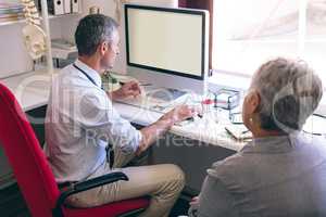 Male doctor discussing over computer with senior woman