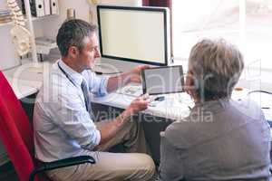 Male doctor discussing over digital tablet with senior woman