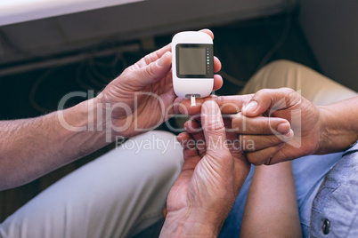 Confident male doctor examining senior female with glucometer
