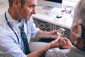 Confident male doctor examining senior woman with glucometer