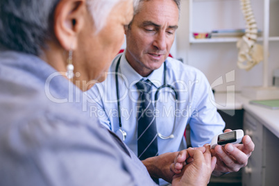 Confident male doctor examining senior woman with glucometer