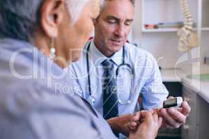 Confident male doctor examining senior woman with glucometer