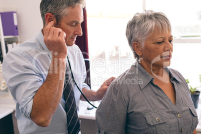 Confident male doctor checking female senior patient in clinic