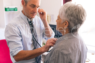 Confident male doctor checking female senior patient in clinic