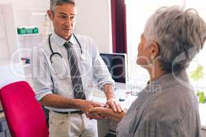 Confident male doctor interacting with senior female patient in clinic