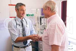 Confident male doctor interacting with senior male patient in clinic