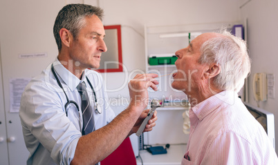 Male doctor checking senior male patient mouth with otoscope