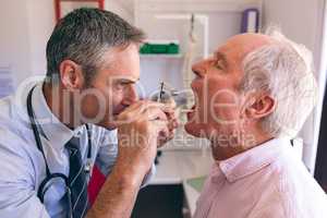Male doctor checking senior male patient mouth with otoscope