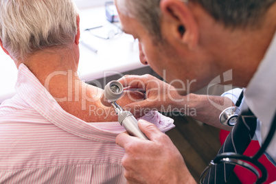 Male dermatologist examining senior patient through dermatoscopy