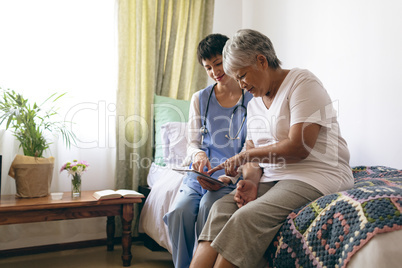 Female doctor and senior female patient using digital tablet at retirement home