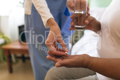 Female doctor giving medicine pill to senior patient