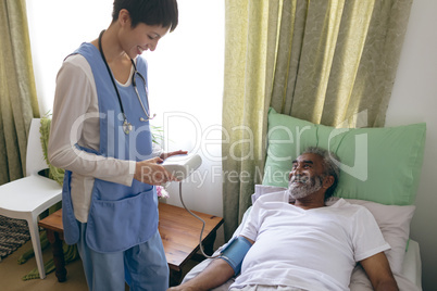 Female nurse checking blood pressure of senior male patient