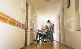Female nurse pushing disabled senior male patient sitting in wheelchair