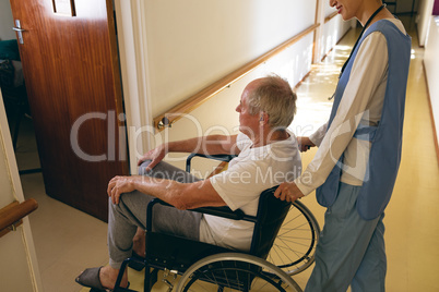 Female nurse pushing disabled senior male patient sitting in wheelchair