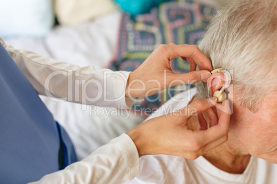 Female nurse applying hearing aid to senior male patient ear