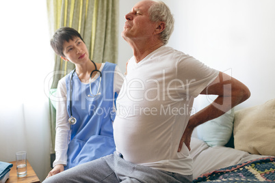 Female nurse helping senior male patient with back pain