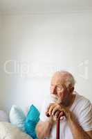 Senior male patient sitting upset on bed with stick at retirement home