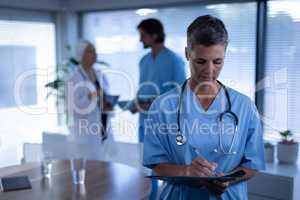 Matured female surgeon writing in medical report in clinic at hospital