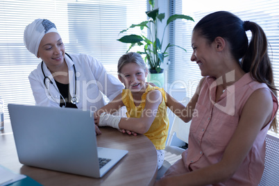 Matured female doctor and mother talking with girl patient in clinic
