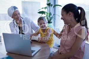 Matured female doctor and mother talking with girl patient in clinic