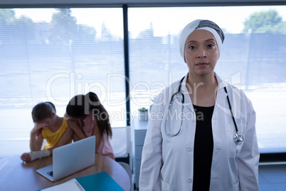 Matured female doctor standing in clinic while mother and doctor sitting upset