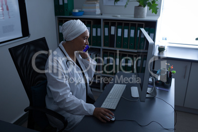 Matured female doctor talking on mobile phone while working with computer